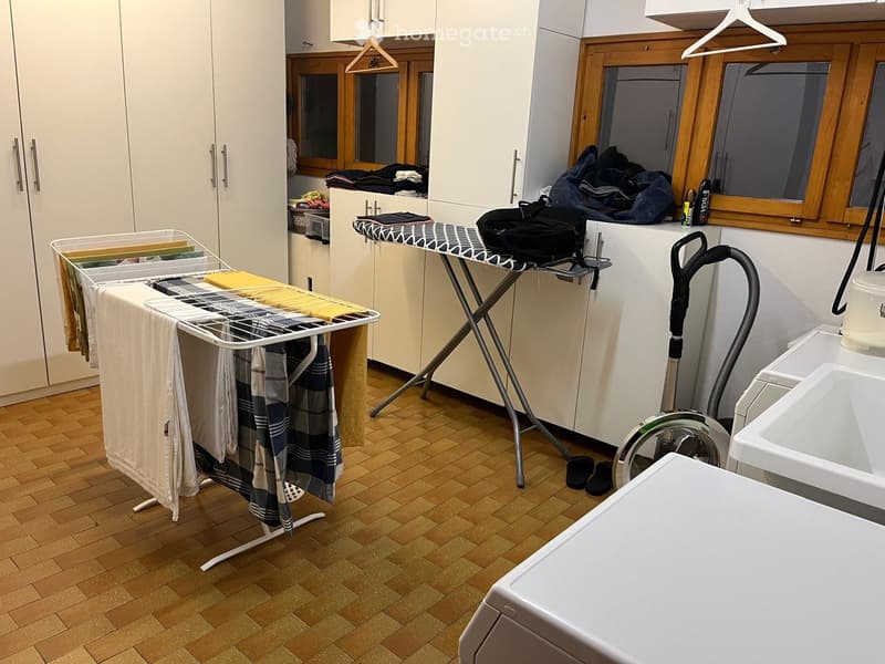 wooden shelves, hanging clothes, ironing board, clothes on the washing machine, white washer and dryer