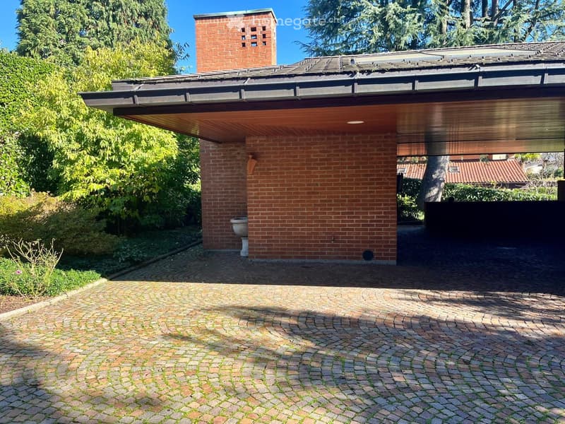 Cobblestone driveway leading to brick garage with chimney, outdoor toilet, and metal canopy