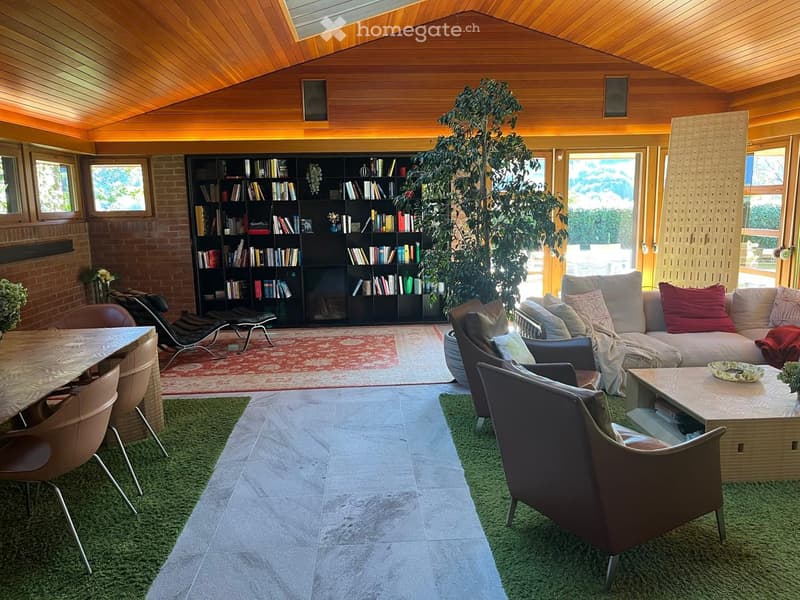 Wooden ceiling, book shelves, couch, armchairs, coffee table, large carpet, dining table, chairs, windows
