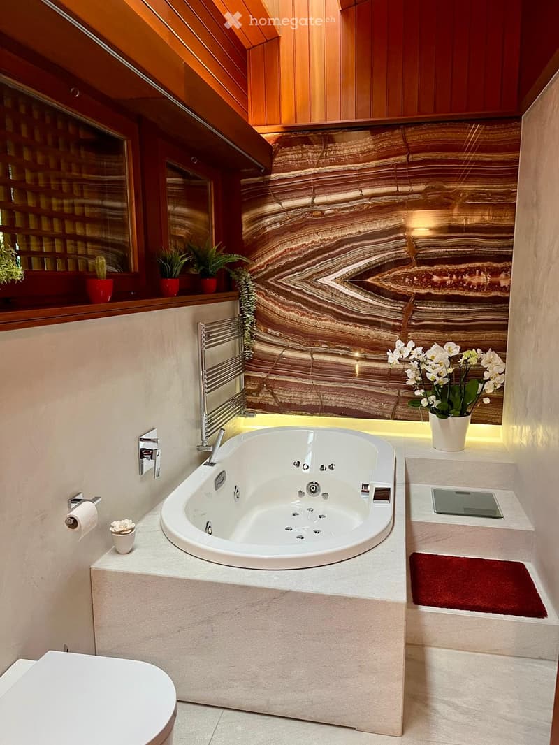 Luxurious bathtub, marbled wall, wooden ceiling, red carpets, flower vase, toilet, roll holder