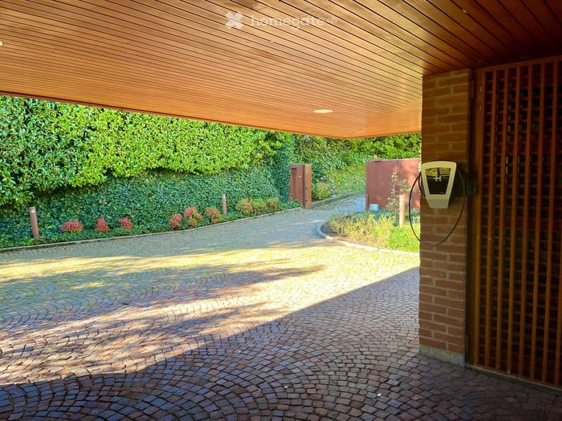 Brick driveway, covered with wooden ceiling, EV charging station, hedge