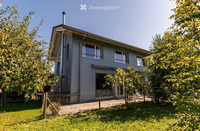 2 story house, gray exterior, large windows, chimney, fenced yard, trees, grass