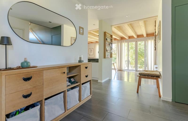 wooden cabinet with drawers, mirror, lamp, stool, wooden floor, white walls, open door leading to another room
