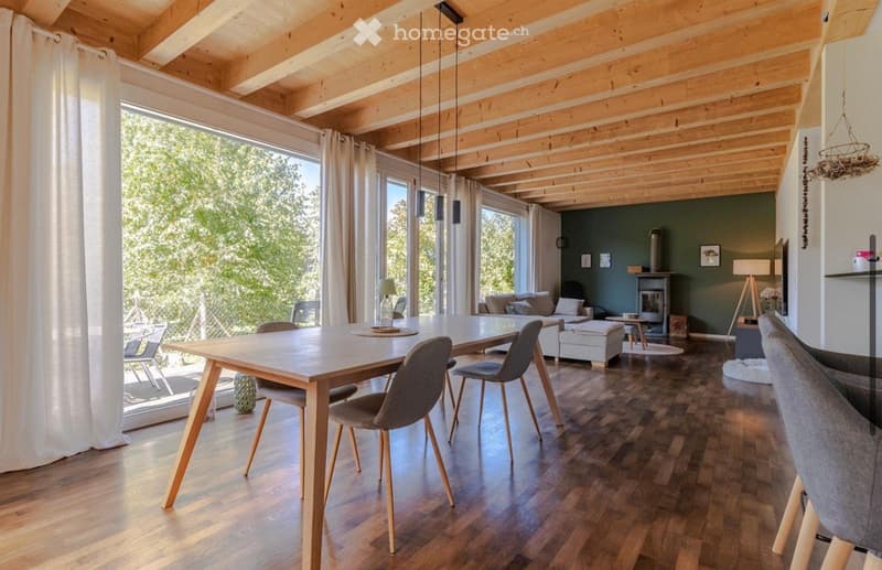 Dining room with wooden floor, large windows, wooden table, chairs, fireplace, couch, and a view of the outside