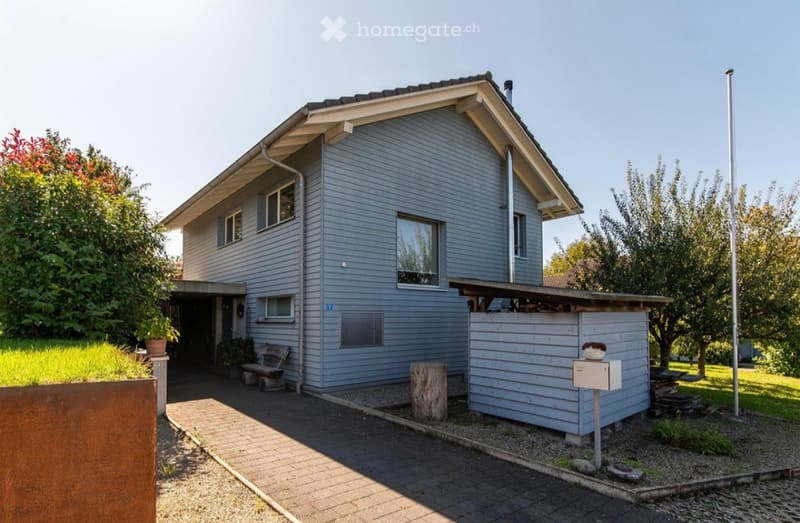 2 story house, blue exterior, brick driveway, wooden bench, mailbox, small shed, trees, plants