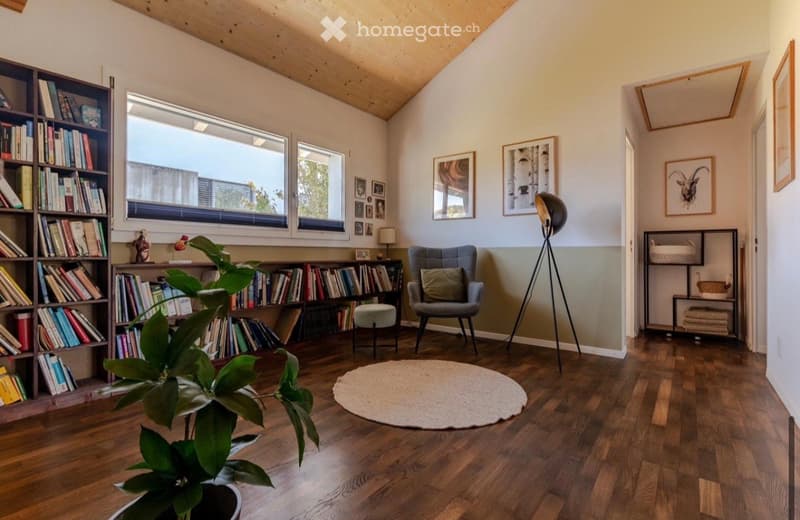 wooden floor, bookshelves, armchair, round rug, plant, lamps, picture frames
