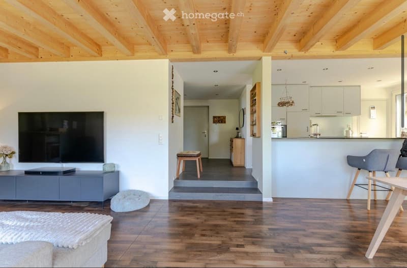 wooden ceiling, wooden floor, white walls, large flat screen TV, entertainment center, kitchen island, stools, dining table, couch, rug