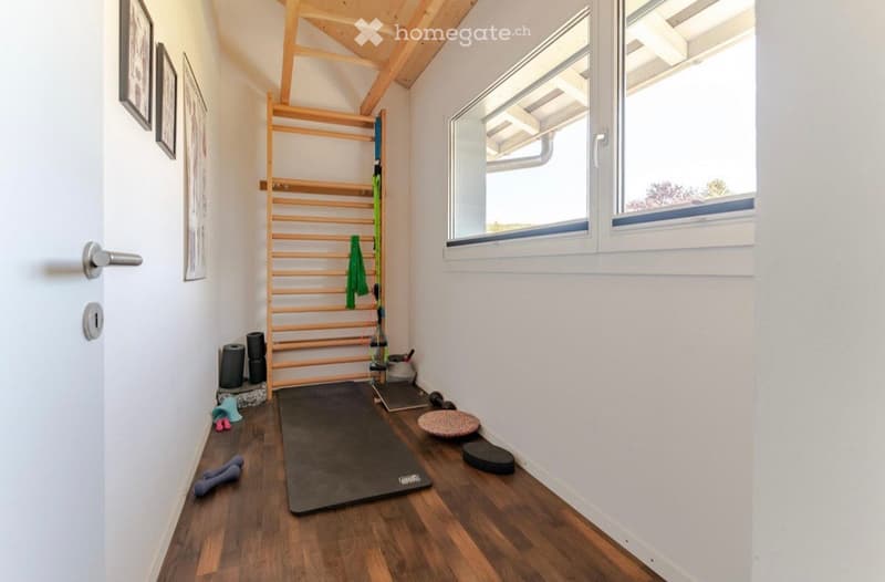 small room with wooden floor, wall mounted rack, yoga mat, dumbbells, and other exercise equipment