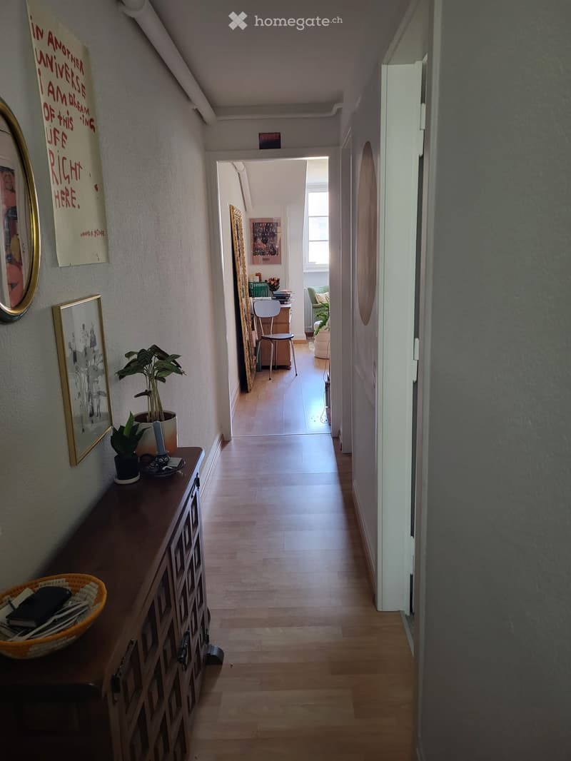 wooden floor, hallway, wooden cabinet with plants, framed pictures on the wall, open door