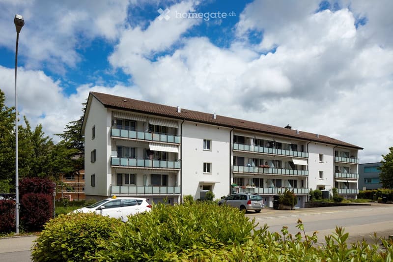 4 story apartment building, white exterior, brown roof, balconies, parking area