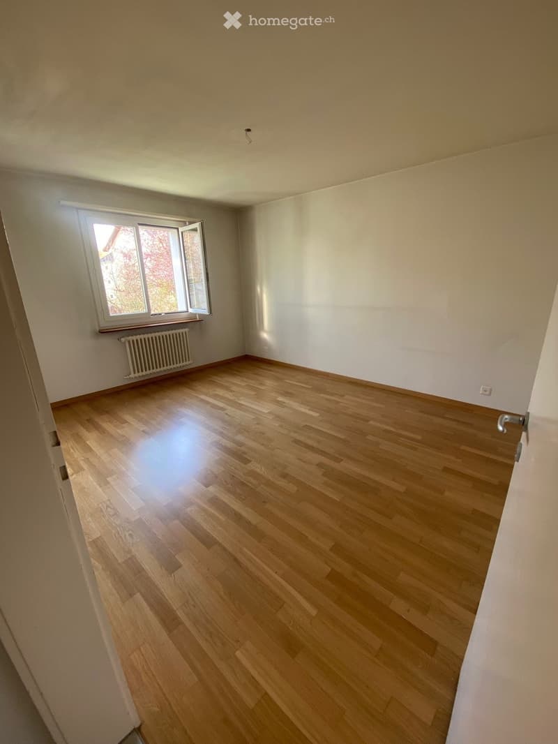 Empty room with wooden floor, white walls, large window, white radiator, power outlet