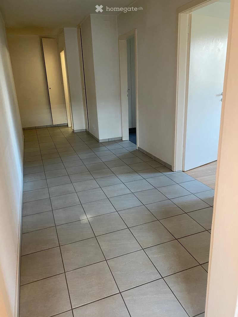 Empty hallway with tiled floor, white walls, and doors leading to different rooms.