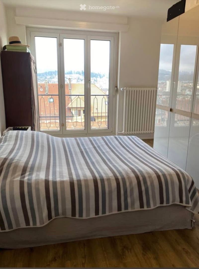 Bedroom with bed, wooden floor, large windows with balcony, wardrobe, radiator, hat on a cabinet
