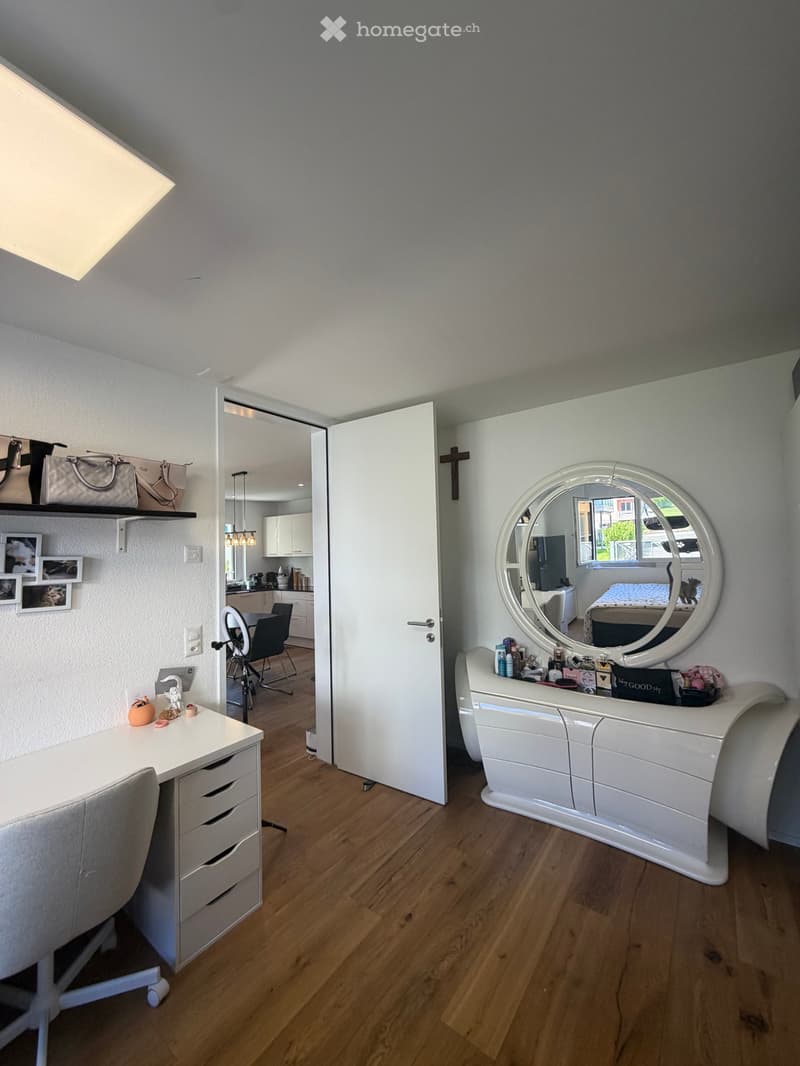 A room with a desk, chair, mirror, and shelves with various items