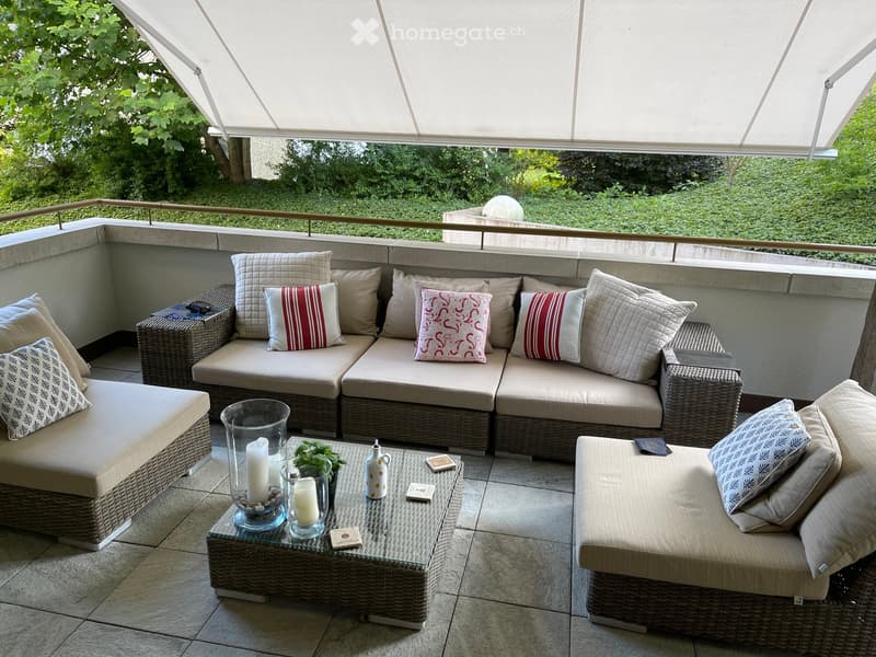 Outdoor patio with wicker furniture, glass coffee table, pillows, and a white awning