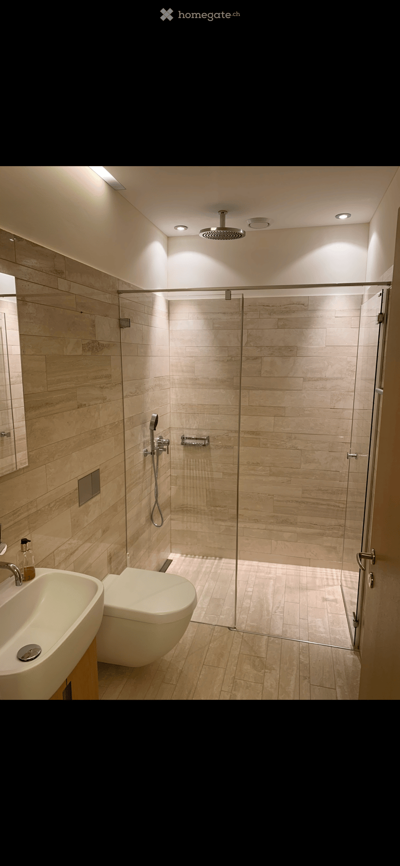 modern bathroom with walk-in shower, white toilet, white sink, wooden floor, beige tiles, mirror, shower head, faucet