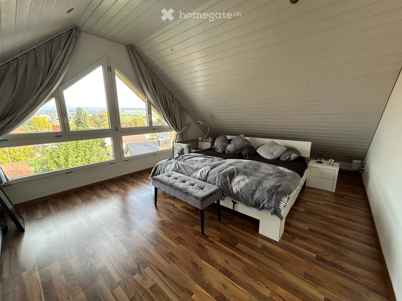 bedroom with double bed, grey bench, white furniture, wooden floor, triangular windows, bright