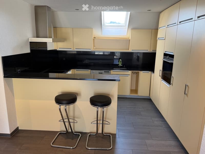 modern kitchen with black countertops, yellow cabinets, stainless steel appliances, two bar stools, skylight