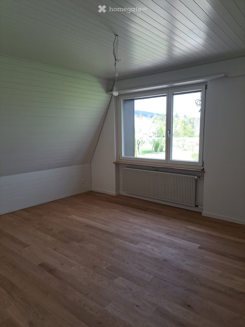 empty room, wooden floor, white walls, large window, radiator, slanted ceiling