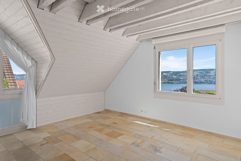Bright, empty attic room with wooden beams, white walls, tiled floor, and large windows offering scenic views.