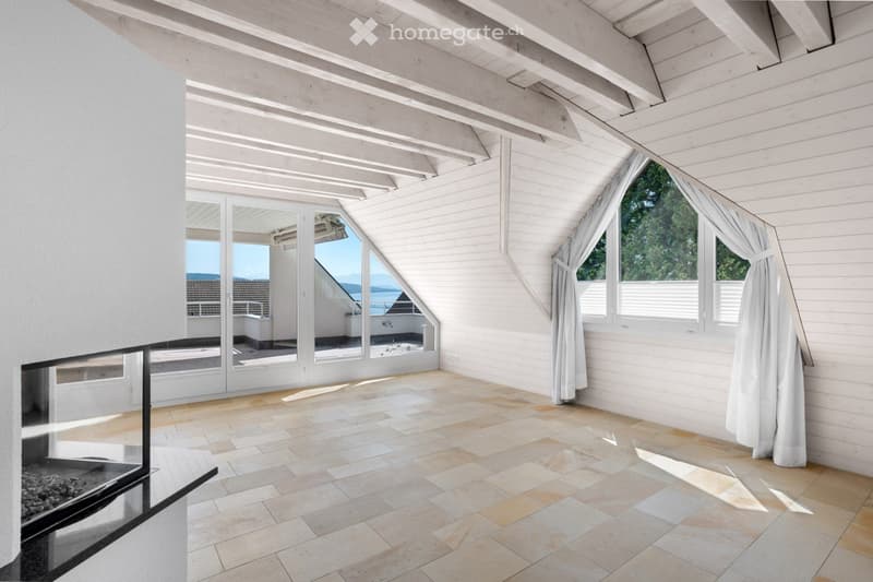 Bright, airy attic space with exposed wooden beams, large windows, and a fireplace. The room features a tiled floor and has a view of the sea through the windows.