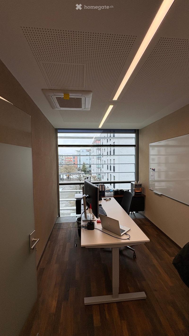 Office room with desk, chairs, monitors, laptop, whiteboard, wooden floor, large window