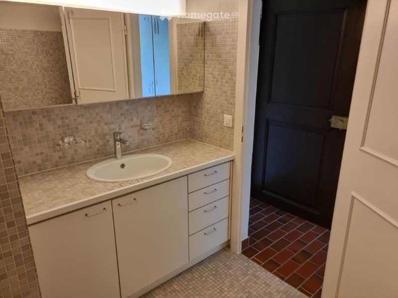 Bathroom with sink, mirror, cabinets, tiled floor, and a door