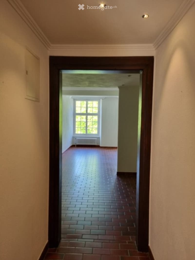 Empty hallway with red brick floor, white walls, and a window with white frame