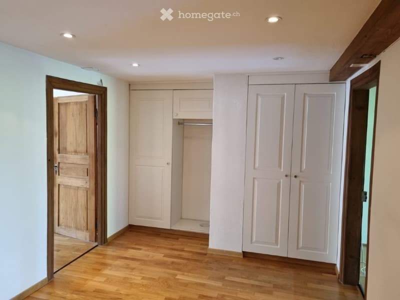 Empty room with wooden floor, white walls, wooden door, built-in wardrobes, and a small closet.