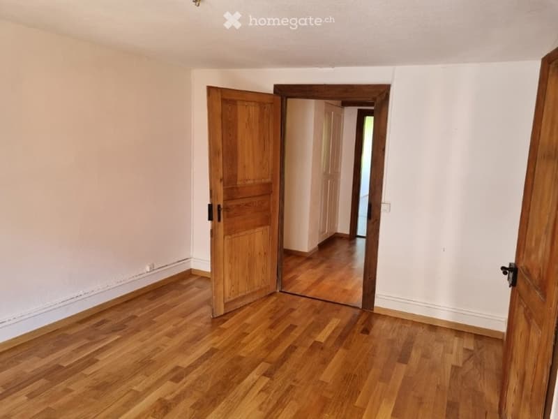 Empty room with wooden floor, white walls, wooden doors, and a mirror