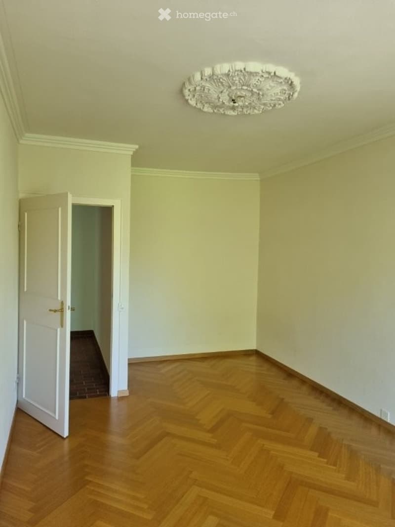 Empty room with wooden floor, white walls, and an open door leading to another room.