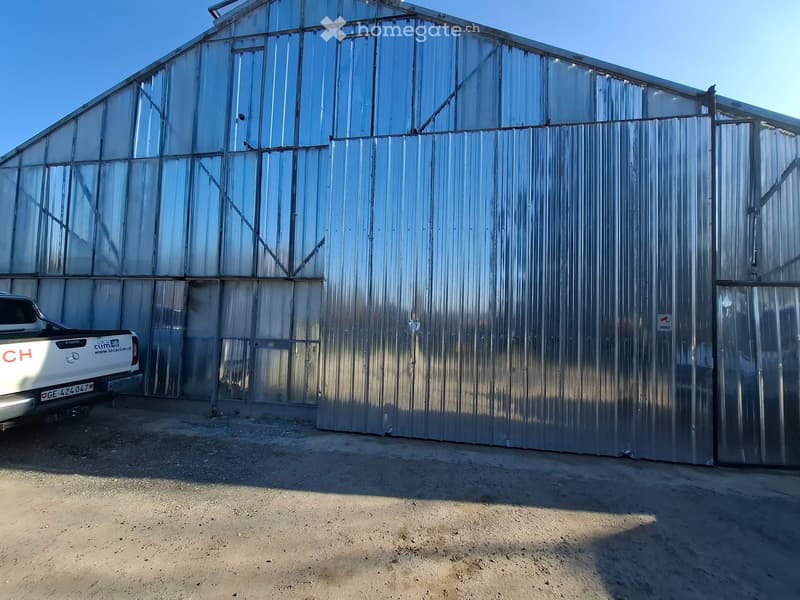 Large metal building with glass windows, open door, white pickup truck parked in front