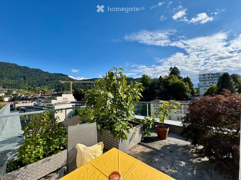 Balcony with table, chairs, plants, and a view of the city and mountains
