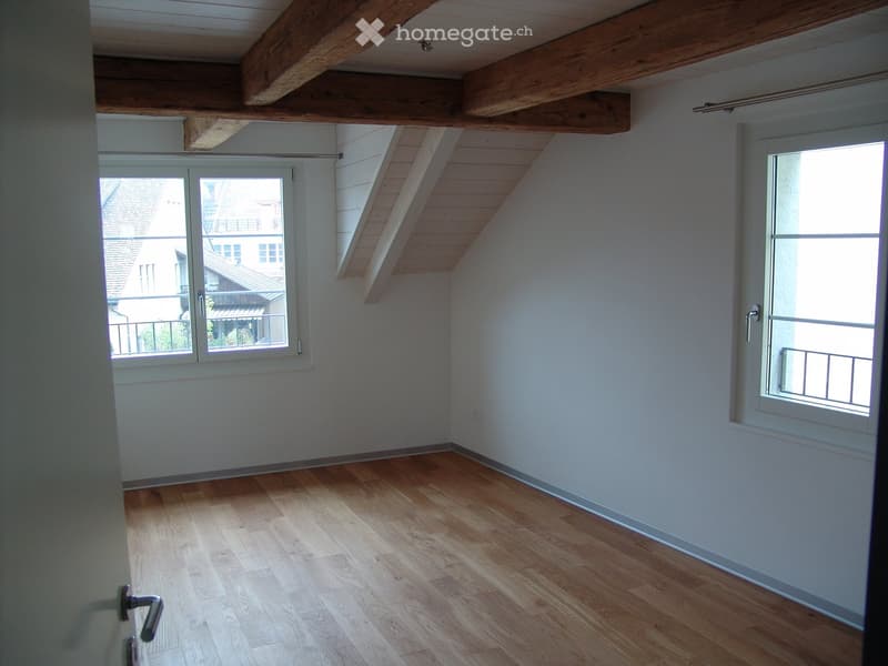 empty room, wooden floor, white walls, wooden beams, two windows, balcony