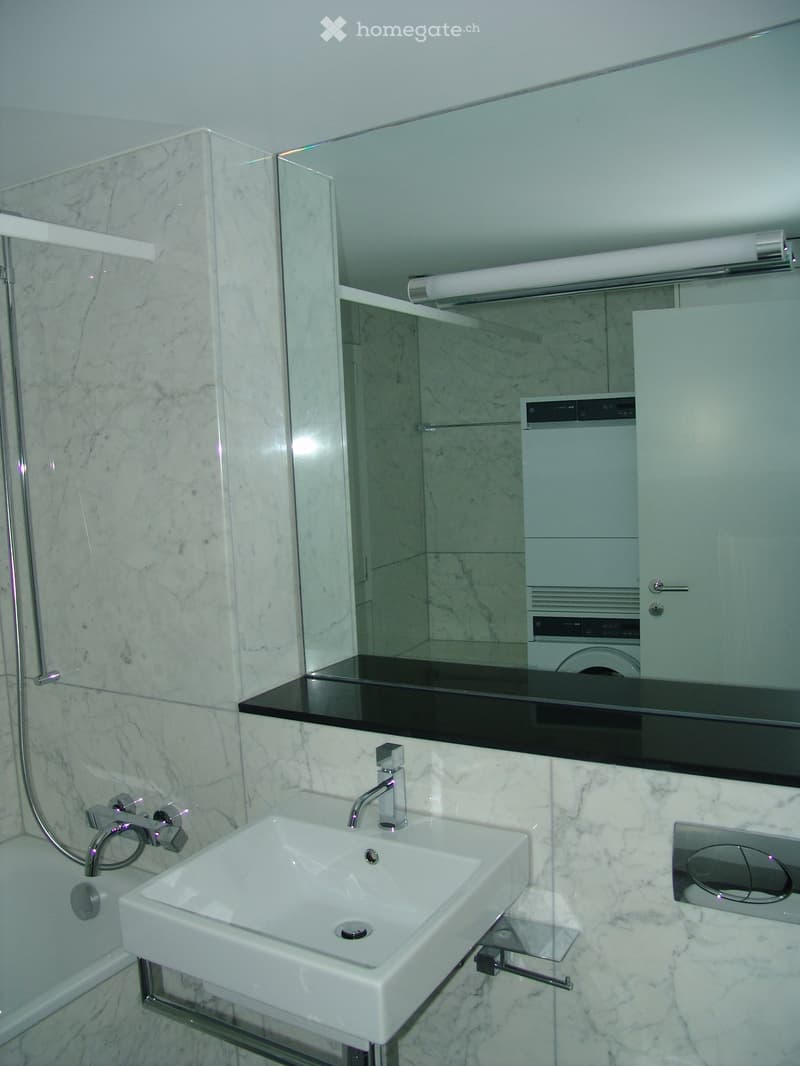 Bathroom with white marble walls, white sink, mirror, bathtub, and washing machine