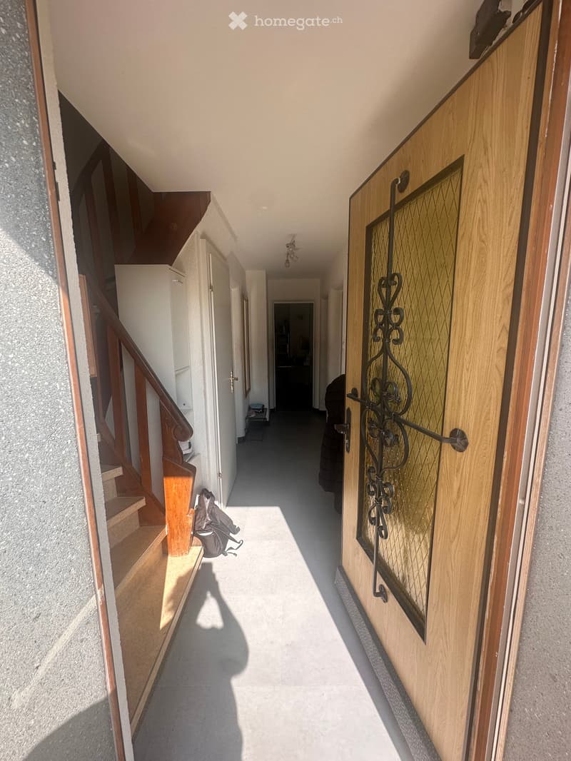 Entrance hallway with wooden door, wooden stairs, tiled floor, white walls, wooden handrail, small table, mirror, and ceiling lights