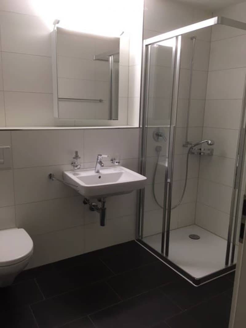 Bathroom with white tiles, white sink, white toilet, glass shower enclosure, mirror
