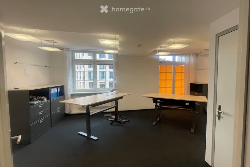 empty room with two desks, cabinets, windows, and ceiling lights