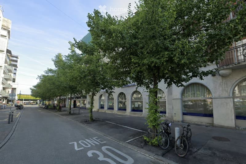 A street with trees, bicycles parked, and a building with arched windows and a balcony.