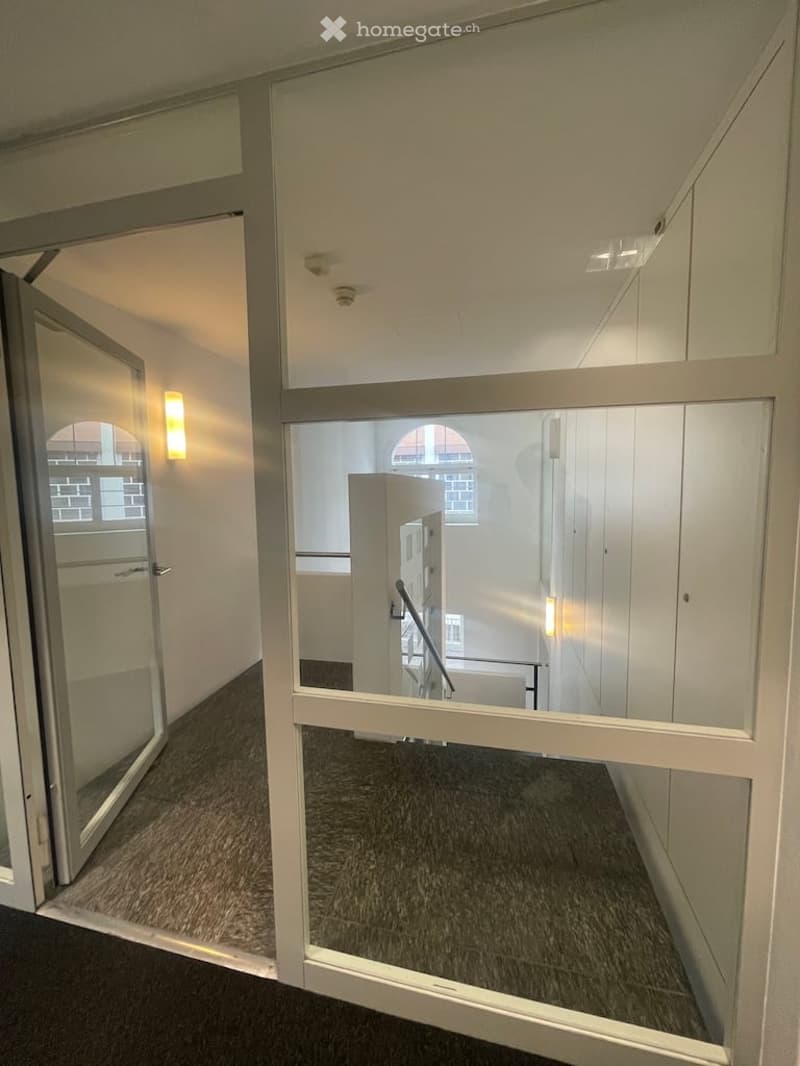 Empty room, glass door, glass wall, carpeted floor, white walls, ceiling lights, metal handrail
