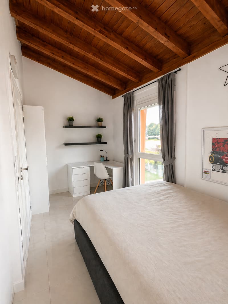 Bedroom with wooden ceiling, white walls, white tiled floor, bed, desk, chair, shelves with plants, window with curtains, picture frame
