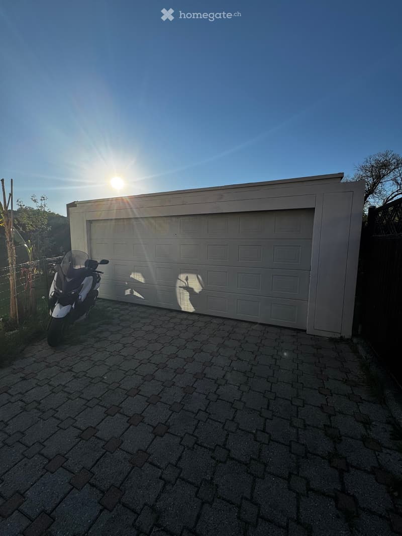 Building. A white garage with a white door and a motorcycle parked in front of it.