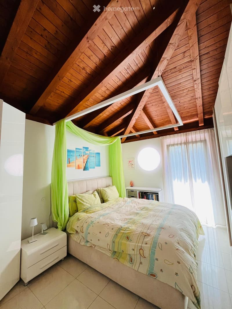 Bedroom with wooden ceiling, bed, nightstand, lamp, and window with curtains
