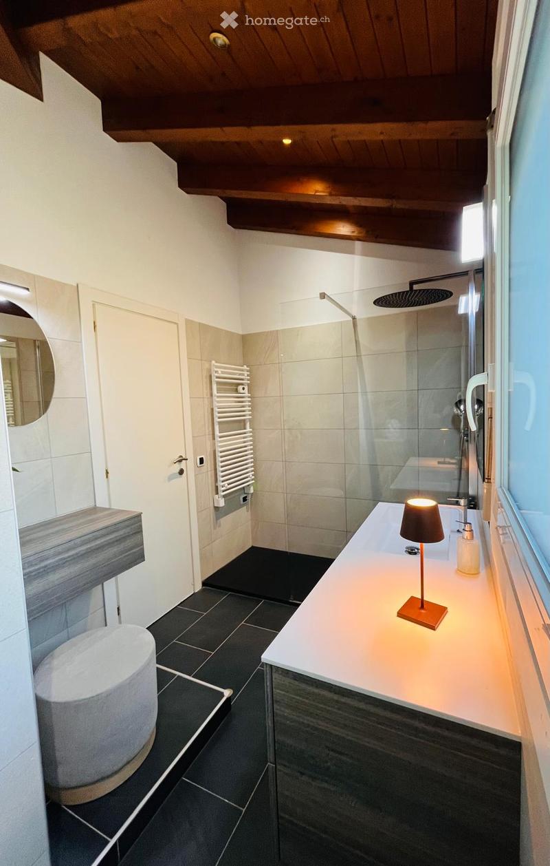 modern bathroom with white tiles, black tiles on the floor, white sink, lamp, mirror, glass shower enclosure, towel rack