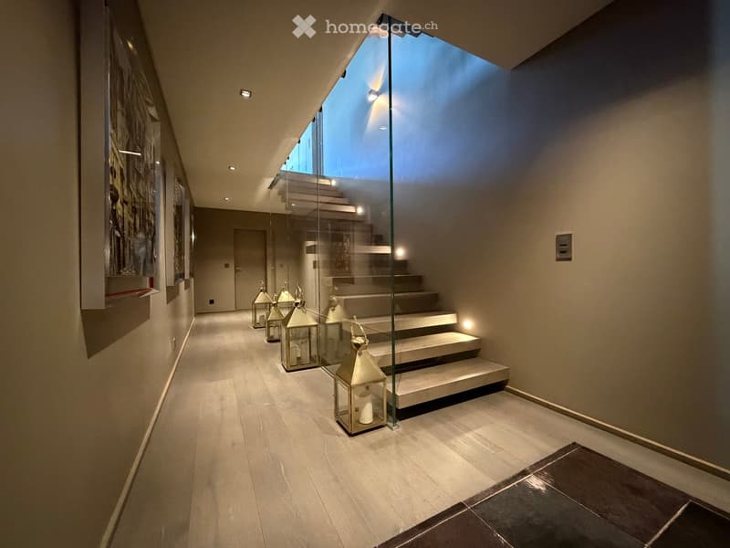 Modern hallway with sleek glass staircase, recessed lighting, and decorative lanterns placed along the floor.