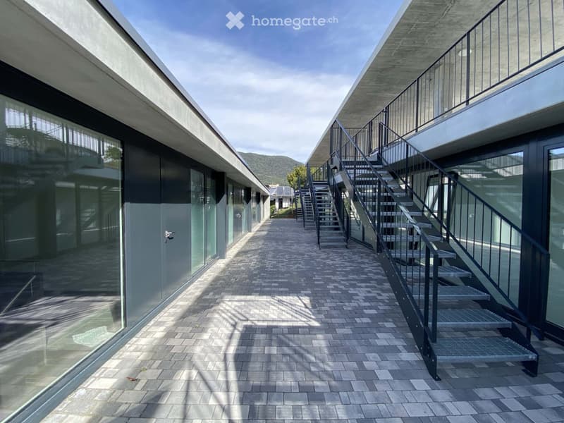 modern concrete buildings, large glass windows, gray brick walkway, stairs leading to balcony, gray railings
