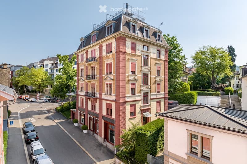 5 story building, red brick, white windows, balconies, cars parked on street