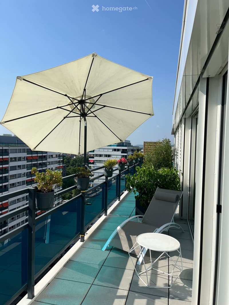Balcony with a large umbrella, lounge chair, small table, and potted plants