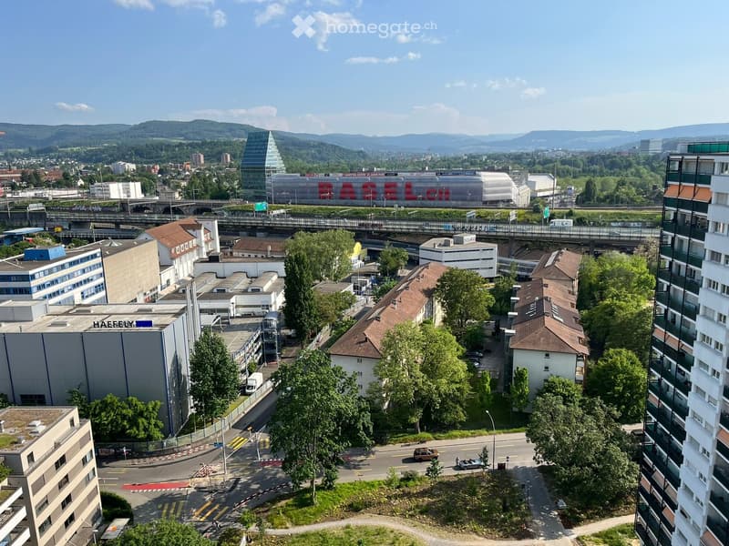 Aerial view of a city with multiple buildings, a shopping center, a bridge, and a road with cars