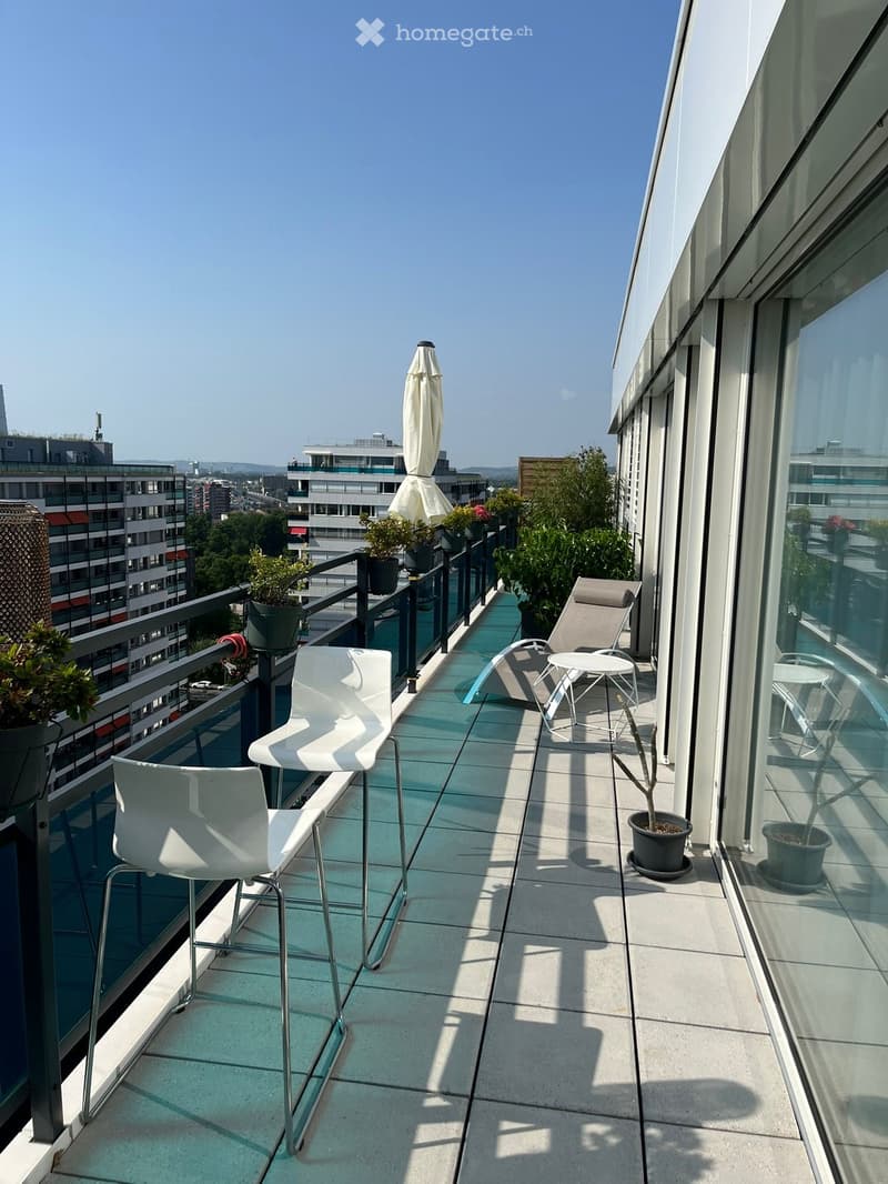 Balcony with white chairs, lounge chair, table, and potted plants, with a view of the city